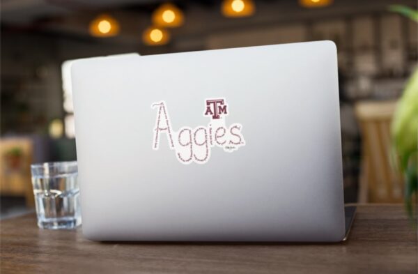 Aggies created with hand-printed Bible verses in maroon ink on a white background with the official ATM logo on a sticker shown on a laptop